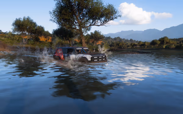 An off-road vehicle drives through a shallow river, creating splashes, with trees and mountains nearby.