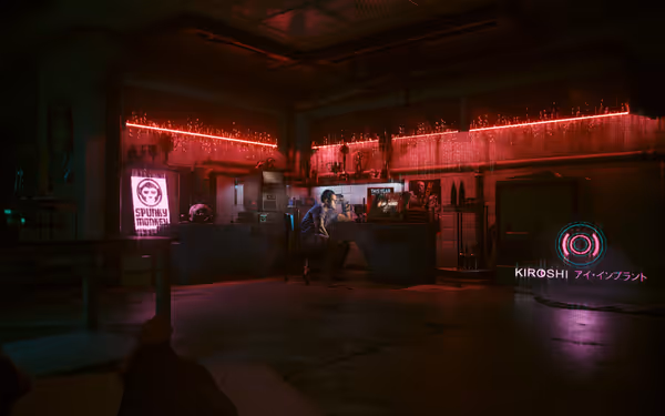 A man sits at a cluttered workstation in a dimly lit, neon-lit cybernetic lab.
