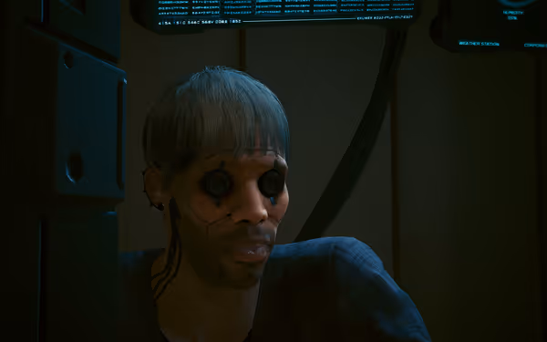 A man with cybernetic eyes and facial implants sits under dim blue lighting.