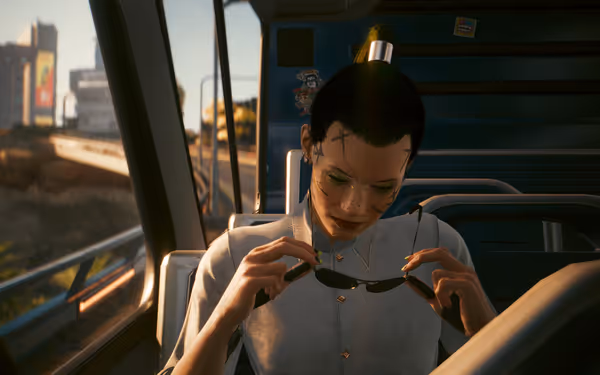 Woman with facial cybernetics looks down at sunglasses while seated on a train.