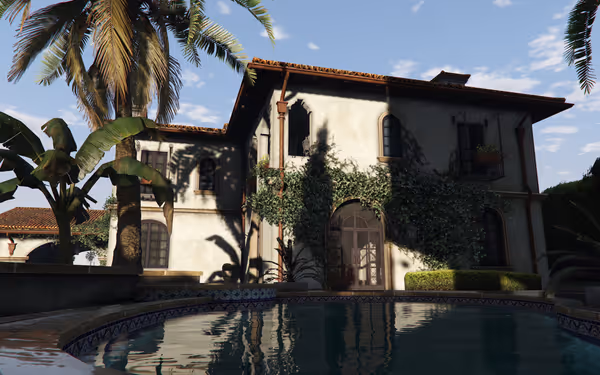 A large Mediterranean-style villa with ivy-covered walls stands beside a calm swimming pool.