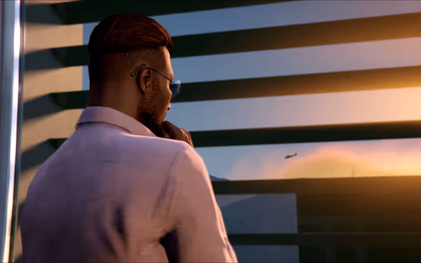 A man in sunglasses and a pink shirt looks out at a sunset through blinds.