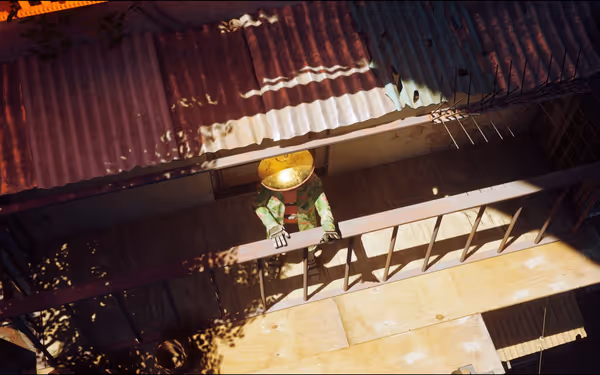 A small robot with a large golden head stands on a balcony in bright sunlight.